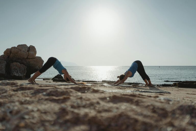 Two women practicing yoga at dawn on a serene beach with clear waters.